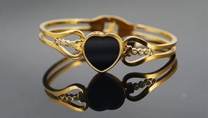 Detailed close-up of a golden heart bangle with black enamel and small white crystals