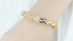 Dettaglio di un bracciale dorato a zigzag con pietre incastonate su un polso donna