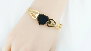 Detail of gold-plated bangle featuring a black heart and sparkling crystal wings on hand