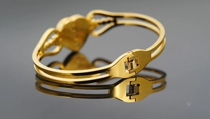 Detail of the golden heart bangle showing a precise mechanical spring clasp mechanism