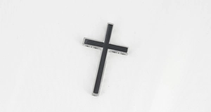 Dettaglio macro di un ciondolo a croce minimalista in acciaio con intarsio in smalto nero