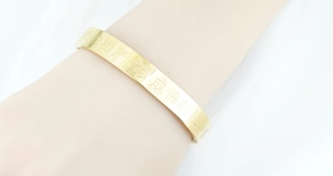 Nahaufnahme eines goldenen Titanstahl-Armreifs mit eingravierter buddhistischer Schrift