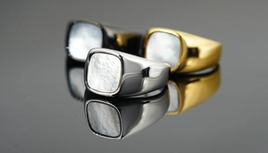 Anillos de sello de acero de titanio en tres colores con nácar sobre superficie de espejo
