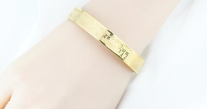 Detailaufnahme eines goldenen Titanstahl-Armreifs mit eingravierten buddhistischen Mantras