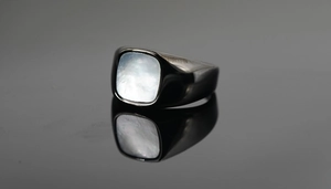 Detalle macro de un anillo de acero negro cepillado con incrustación de nácar blanco