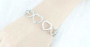 Gros plan d'un bracelet cœur en argent avec strass pavés au poignet d'une femme