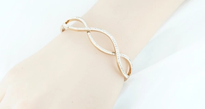 Detail of rose gold wave bangle with pavé-set zircons worn on wrist in bright studio setting