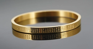 Detail eines goldenen Edelstahl-Armreifs mit eingraviertem buddhistischem Herz-Sutra