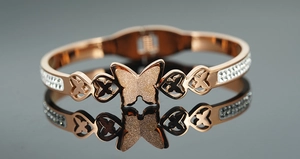 Dettaglio macro del bracciale rigido a farfalla in oro rosa con cristalli e trama opaca