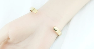 Close-up of a minimalist golden open bangle with polished mirror finish on a wrist
