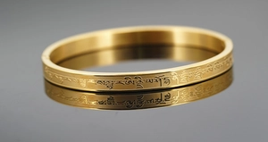 Macro shot of gold-plated bangle with detailed Sanskrit engravings on a reflective surface