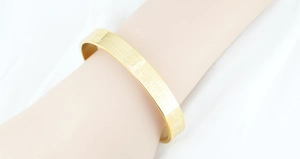 Macro shot of gold-plated stainless steel open cuff bangle with engraved heart sutra