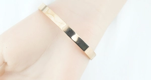Polished rose gold stainless steel flat bangle with star pattern worn on wrist