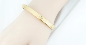 Macro shot of gold plated titanium steel bangle featuring engraved Sanskrit mantra pattern
