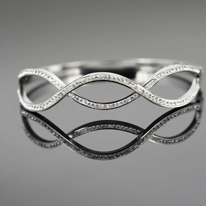 Polished silver infinity wave bangle with zircon inlay on a dark reflective surface