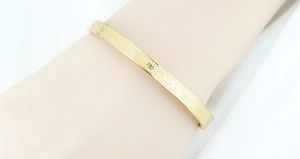 Detailed close-up of golden stainless steel bangle with engraved religious scriptures