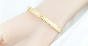 Detail of gold titanium steel bangle with engraved Buddhist mantras and clasp closure