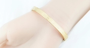 Close-up of golden stainless steel open bangle with engraved LV patterns and motifs