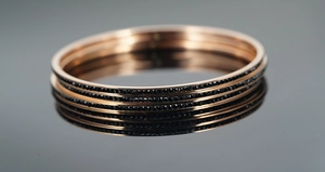 Gros plan de trois bracelets en titane or rose sertis de pierres noires sur surface réfléchissante