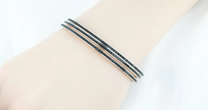 Détail de trois joncs en or rose avec diamants noirs sur poignet montrant le style empilé