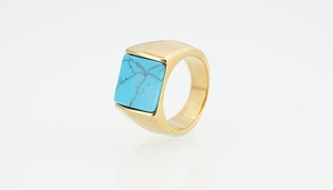 Vue détaillée de la bague chevalière dorée avec pierre turquoise carrée et texture naturelle