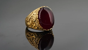 Macro side view of vintage gold ring with dark red oval stone and ornate engraving