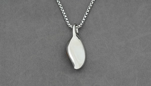 Close-up of a silver-tone leaf pendant with a box chain on a grey textured fabric