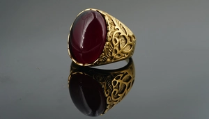 Macro shot of vintage gold steel ring with red oval gemstone and ornate hollow patterns