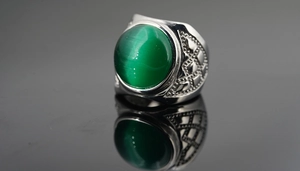 Vue macro d'une bague argentée vintage avec une grande pierre œil de chat verte et gravures