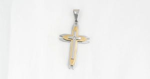 Détail du pendentif croix bicolore argent et or avec cristal central sur tissu blanc