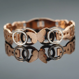 Rose gold butterfly bangle with micro-pave crystals and frosted finish on a dark background