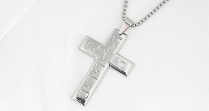 Detailed close-up of a silver stainless steel cross pendant with Greek key pattern details