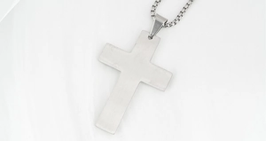 Close-up of brushed stainless steel cross pendant featuring unique Greek key pattern engraving