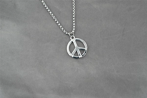 Vue détaillée du pendentif symbole de paix argenté avec chaîne sur tissu gris