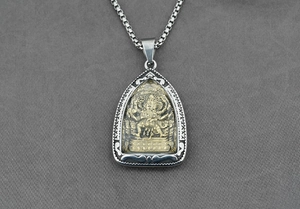 Dettaglio macro del ciondolo amuleto Buddha con rilievo dorato su catena d'argento