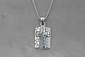 Macro shot of silver square cross pendant with industrial textured relief and snake chain