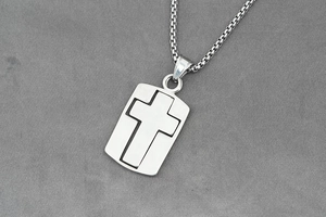 Close-up of silver box chain necklace with square cross pendant on grey fabric