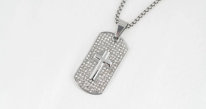 Detailopname van glanzende kruis hanger met witte kristallen en roestvrijstalen ketting
