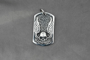 Detailed close-up of a silver gothic skull pendant with wings and vintage texture