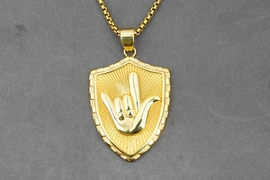 Vista de detalle del colgante de escudo dorado con gesto de mano en cadena de acero
