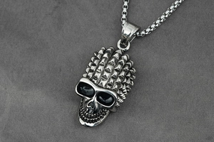 Macro shot of a punk-style silver skull pendant with rivet details and a box chain necklace