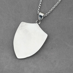 Collar con colgante de escudo en acero de titanio pulido y cadena box sobre tela gris