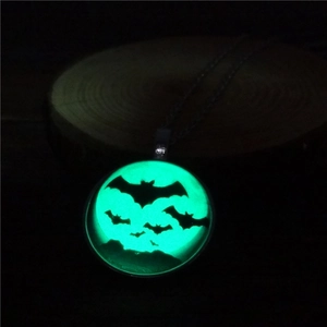 Macro shot of luminous green bat pendant glowing brightly in complete darkness