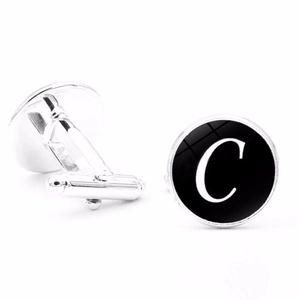 Close-up of silver men's cufflinks featuring a black round glass face with white letter C
