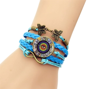 Detail of layered woven bracelet featuring bronze butterfly, infinity charm, and evil eye motif
