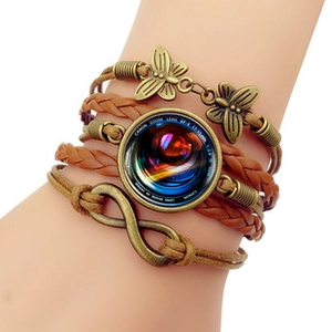 Macro detail of the woven leather bracelet featuring a bronze butterfly and camera lens motif