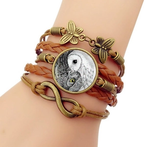 Detail of multi-layer leather bracelet featuring Aztec sun stone owl glass gem and charms
