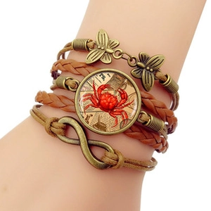 Detail of multi-layer woven leather bracelet featuring red crab charm and butterfly accents