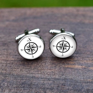 Detailed view of silver polished compass cufflinks with N E S W marks on a wood surface