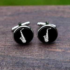 Detail of silver saxophone cufflinks with black face on a rustic wooden surface